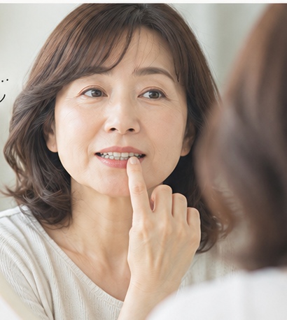 鏡を見ながら口元を気にする50代女性